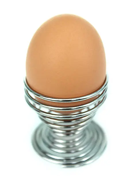 Photo showing a soft boiled egg sitting in a stylish silver / chrome metal egg-cup that is made to look like a coiled spring, photographed looking down from above.  The chicken egg is pale brown in its appearance and has been served at breakfast time, ready to be accompanied by an army of toast soldiers with butter.