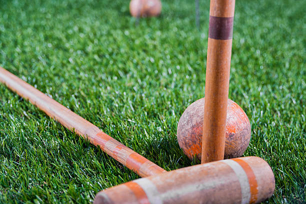 A Vintage Croquet Mallet and ball with a orange and white stripe sitting in the grass, the ball resting against the peg, 