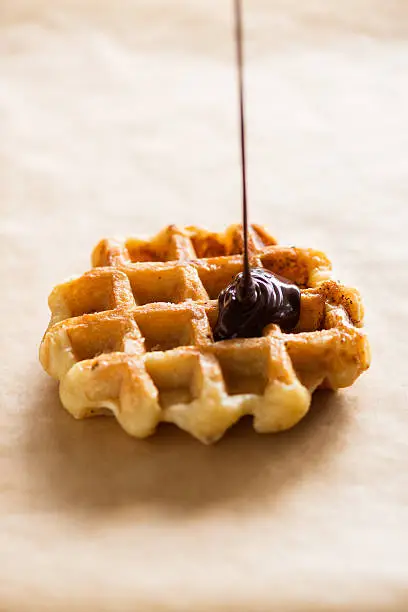 Photo of Liquid Chocolate Ganache Dripping onto Belgium Waffle, Parchment Paper Background