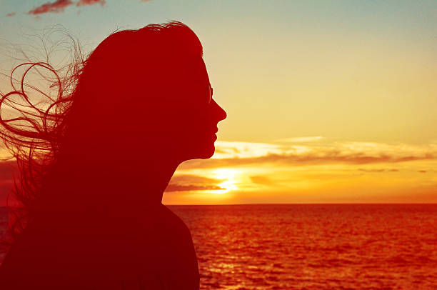 Single adult woman silhouette with sunglasses at Pacific ocean Sunset with flying hair