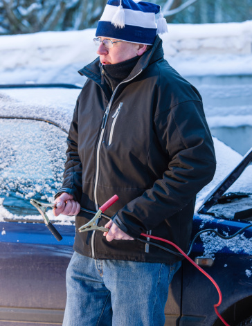 A man waits help with the booster cables beside the car, cold winter day