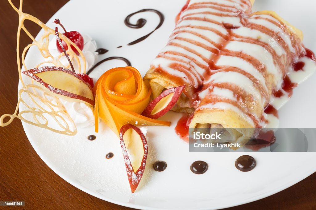 Pancakes with cherry jam Pancakes with cherry jam beautifully decorated with flowers of fruit and chocolate on a white plate, which stands on a wooden table near the window in the interior cozy cafe. Shallow depth of field. 2015 Stock Photo