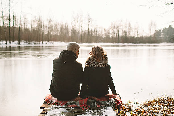 A couple sitting on a pier above a frozen lake stock photo