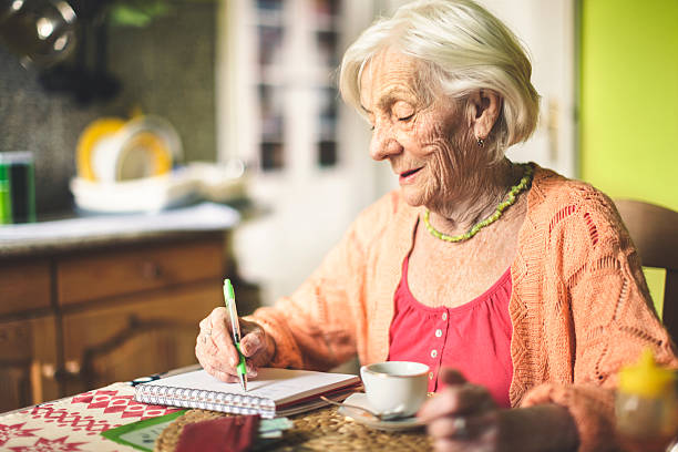 sênior mulher cálculo de finanças na sua cozinha - check writing currency finance - fotografias e filmes do acervo