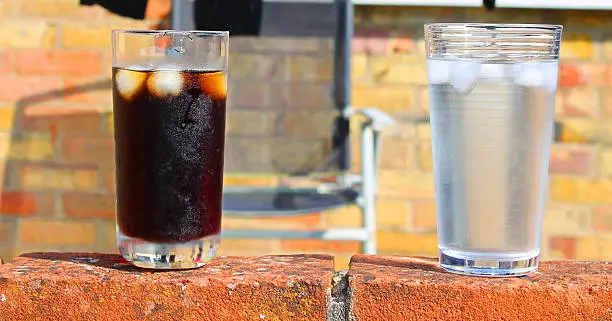 Two full glasses with beverages sit on a brick wall