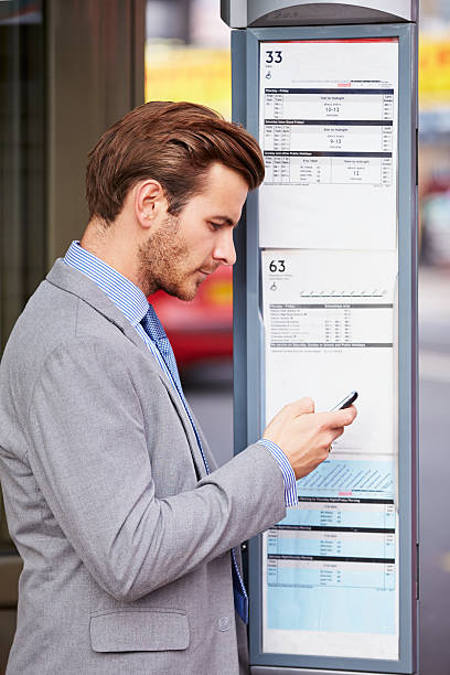 istock Businessman At Bus Stop With Mobile Phone Reading Timetable 466715463