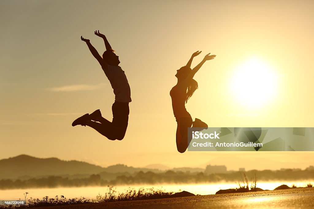 Fitness couple jumping happy at sunset Fitness couple jumping happy at sunset with the sun in the background Couple - Relationship Stock Photo