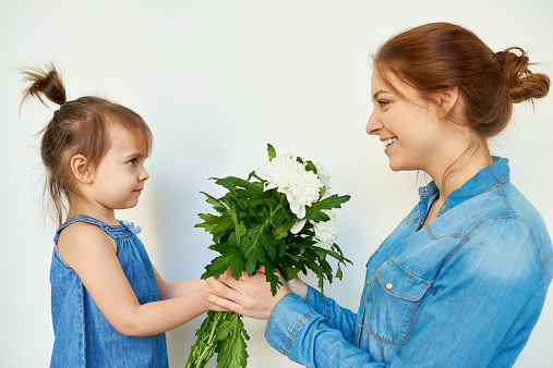 Young women receiving bunch of white chrysanthemum from her little daughter on Mother's day