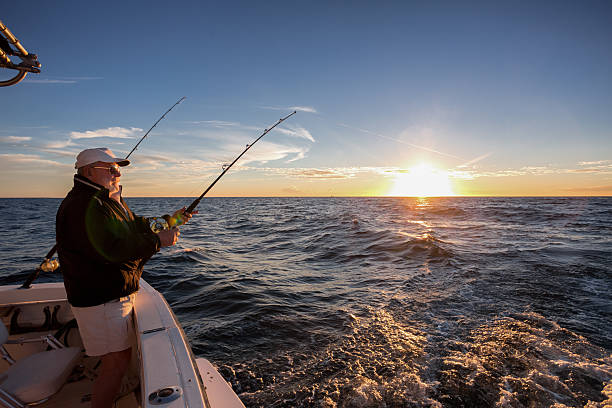 Elderly Man Fishing Man fishing on the ocean from the back of his boat at sunset fishing rod photos stock pictures, royalty-free photos & images