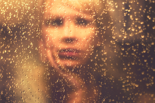 The mirror image of a woman in the window with rain drops