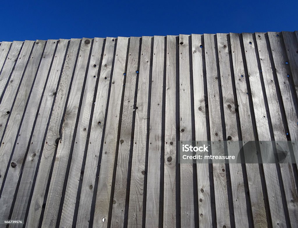 Image of wooden feather-edge fence, treated / tanalised timber feather-edge fencing Photo showing a traditional wooden featherboard fence that is providing a boundary in a suburban back garden, made with feather-edge tanalised timber.  This traditional featherboard fencing tends to be more expensive than larch-lap fence panels, but this structure will last much longer, especially when substantial pre-treated fence posts are used. Fence Stock Photo