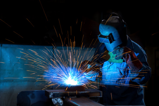 A heavy industry worker kneeling and grinding metal parts in facility.