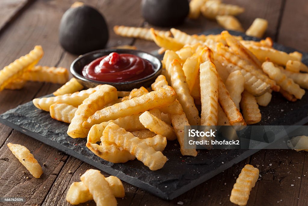 A plate of unhealthy baked crinkle French fries and ketchup Unhealthy Baked Crinkle French Fries with Ketchup French Fries Stock Photo