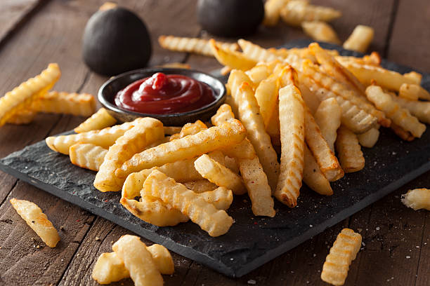 A plate of unhealthy baked crinkle French fries and ketchup Unhealthy Baked Crinkle French Fries with Ketchup french fries stock pictures, royalty-free photos & images