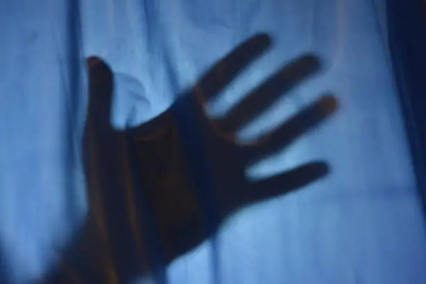 Help concept with hand silhouette behind a curtain.Victim reaching for help behind a curtain.