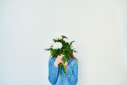 Young woman hiding her face behind bunch of flowers