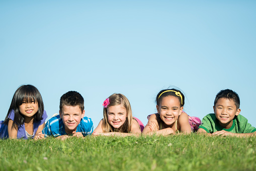 A group of multi-ethnic children playing together and lying in the grass at the park