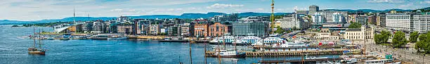 Panoramic vista across the busy waterfront of central Oslo, Norway's vibrant capital city, from the modern redevelopment of Aker Brygge to the broad promenade of Radhusplassen and the blue waters of Pipervika. ProPhoto RGB profile for maximum color fidelity and gamut.