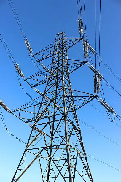 Photo showing a tall high-voltage transmission tower, which is known in the UK and much of Europe as a double circuit electricity pylon.  This photo shows a metal tower from a low angle, looking up, with wires, conductors and insulator strings.  The top part of the structure is named the 'peak', while beneath is the 'cage', 'steel lattice diagonals' and the 'main legs'.