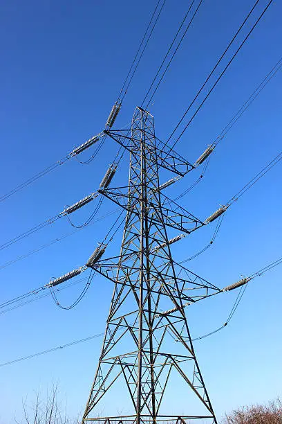 Photo showing a tall high-voltage transmission tower, which is known in the UK and much of Europe as a double circuit electricity pylon.  This photo shows a metal tower from a low angle, looking up, with wires, conductors and insulator strings.  The top part of the structure is named the 'peak', while beneath is the 'cage', 'steel lattice diagonals' and the 'main legs'.