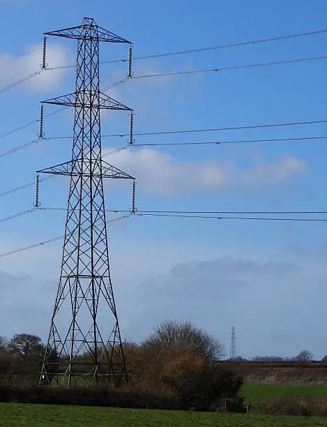 Photo showing a tall high-voltage transmission tower, which is known in the UK and much of Europe as an electricity pylon.  The photo shows a tower, with conductors, insulator strings and cables / wires stretching into the distance.  This part of the structure is close to the top (peak) and known as the 'cage'.