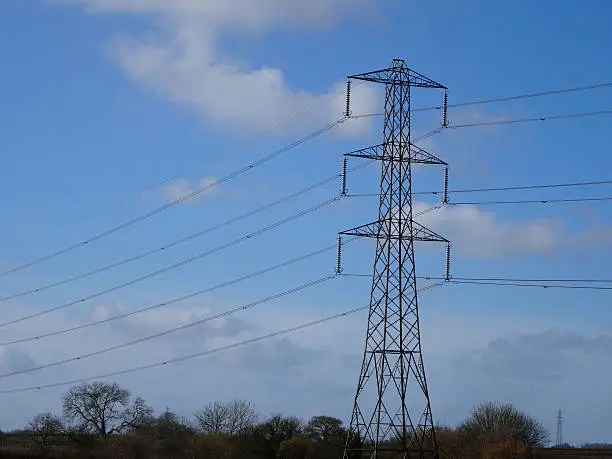Photo showing a tall high-voltage transmission tower, which is known in the UK and much of Europe as an electricity pylon.  The photo shows a tower in the countryside, with conductors, insulator strings and cables / wires stretching into the distance.  This part of the structure is close to the top (peak) and known as the 'cage'.