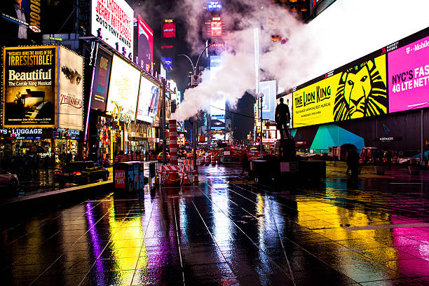 Times Square at Night View of Times Square at night illuminated with neon colors. Wet streets. Broadway plays and chain store ads on billboard. Smoke rises from ground. New York city. theatre district stock pictures, royalty-free photos & images