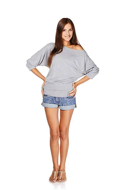 Full length of smiling young slim tanned female in denim shorts standing with hands on hips, isolated on white background