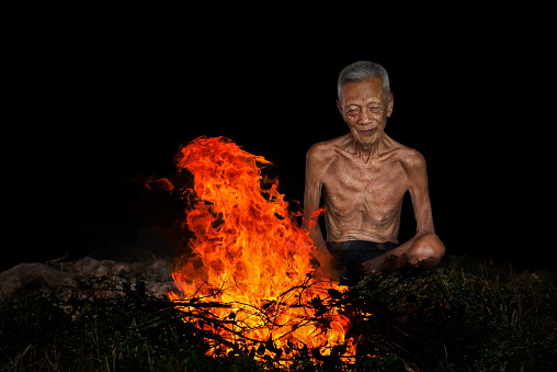 old man sitting next to a fire