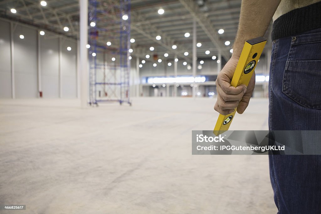Manual Worker Holding Spirit Level In Warehouse Midsection of manual worker holding spirit level in empty warehouse Adult Stock Photo