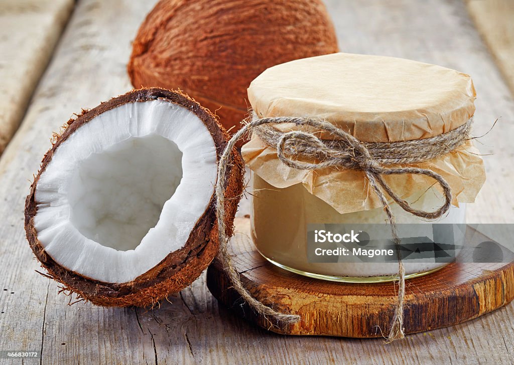 A coconut jar with coconut oil and coconuts sliced in half jar of coconut oil and fresh coconuts on wooden table Coconut Oil Stock Photo