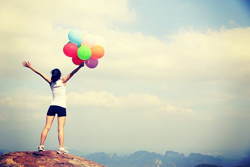 cheering woman with colorful balloons on mountain peak cliff