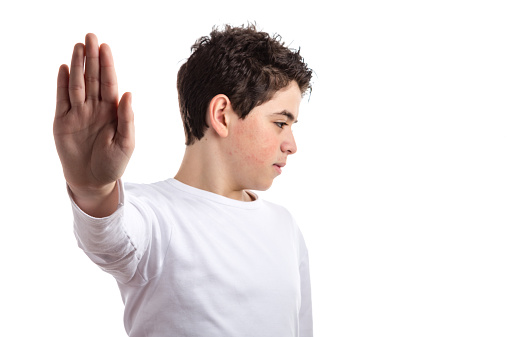 Caucasian teen with acne skin in a white long sleeve t-shirt smiles making Talk to the hand gesture with right hand