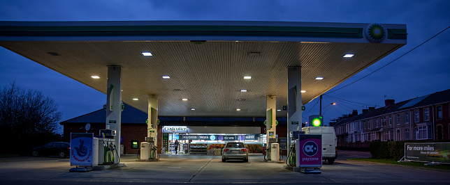 Llanelli, UK - March 15, 2015: Forecourt of BP petrol station at night. The cashier and customer is visible through the window and a man is walking out of the building