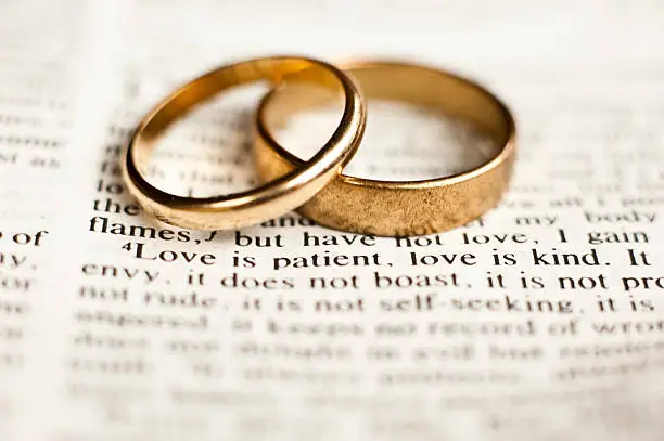 Wedding rings sitting on the 1 Corinthians 13 Bible passage on what love is.