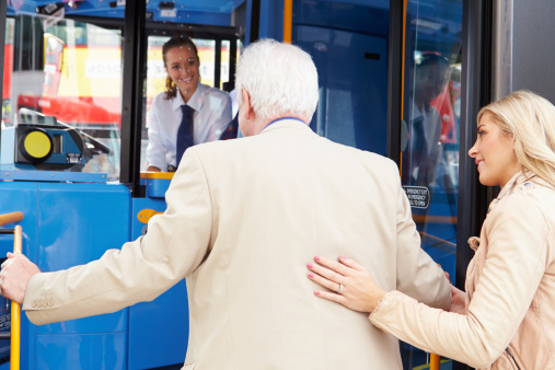 Rear View Of Woman Helping Senior Man To Board Bus