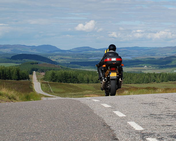 Lone Motorbike Riding in the Highlands A lone motorbike riding on an empty road in the Highlands of Scotland in summer motorized vehicle riding stock pictures, royalty-free photos & images