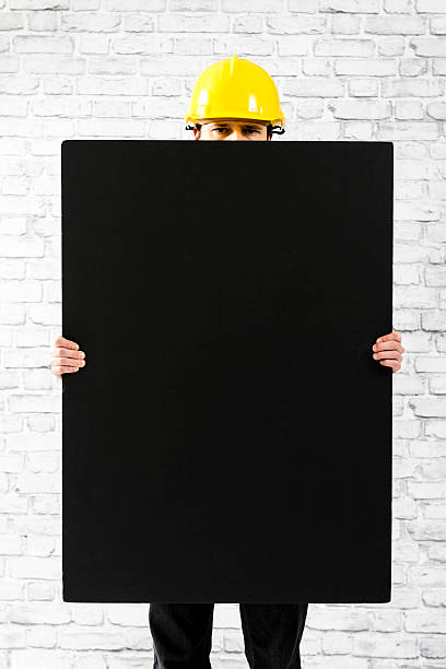 istock Man in yellow helmet holding blank black board, copy space 466854759