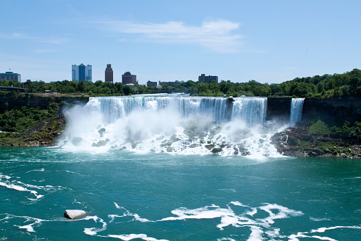 Scenes from the Canada side of Niagara Falls. The light blue skies and blue-green water make this a beautiful outdoor nature landscape. The national park borders Canada and New York State. This shot shows the American side of the falls taken in Canada with part of the Buffalo city skyline in the background. - A great shot taken in the outdoors.