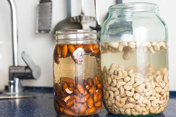 Soaked almonds and cashews in large glass in domestic kitchen. They are used to prepaire raw vegan cheese and other raw recepies.