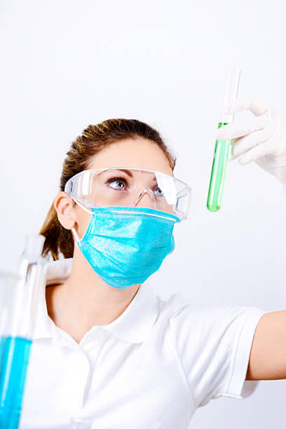 Young female scientist in the lab, examining solutions in test tubes. Woman wearing protective gloves and mask, while working in the medical or research lab. Image shot with Nikon D800 and developed from RAW file.