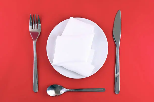 Table serving-knife,plate,fork and silk napkin  on  red colour background.