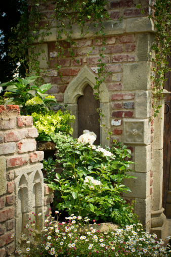 An overgrown mediaeval style building with english country garden flowers,