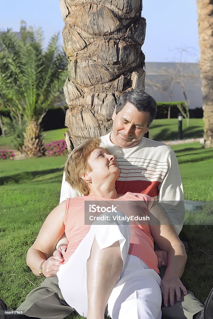 Coppia matura disteso in abbraccio vicino all'Albero di palme. - Foto stock royalty-free di Abbracciare una persona