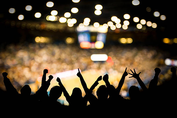 Basketball Excitement Fans excited at basketball game. Silhouetted fans raising arms in celebration at a basketball game. fan enthusiast stock pictures, royalty-free photos & images