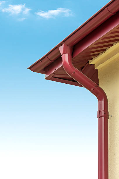 istock Red rain gutter system on a yellow house with a blue sky 466918543