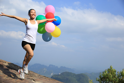 cheering woman running with colorful balloons on mountain peak cliff