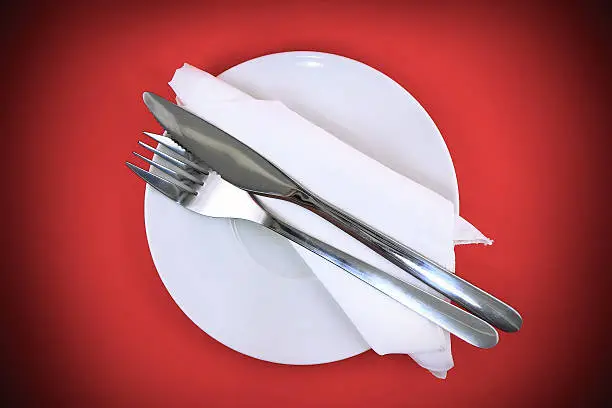 Table serving-knife,plate,fork and silk napkin  on  red colour background.