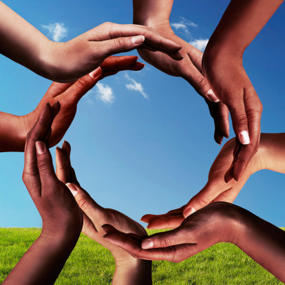 Conceptual peace and unity symbol of different black african ethnicity hands making a circle together on blue sky and green grass background
