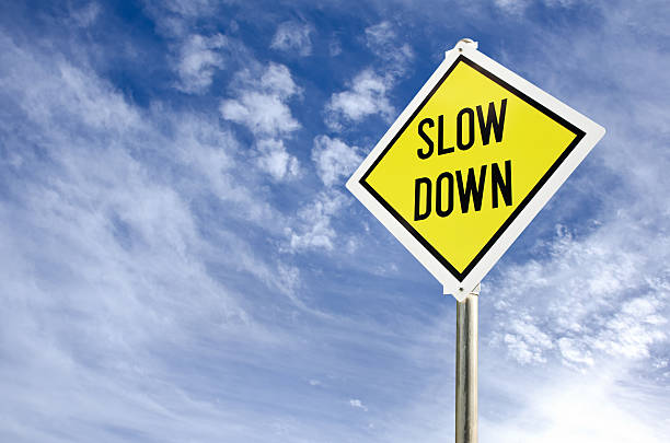 Slow Down road sign Slow Down yellow road sign on blue sky with clouds background slow stock pictures, royalty-free photos & images